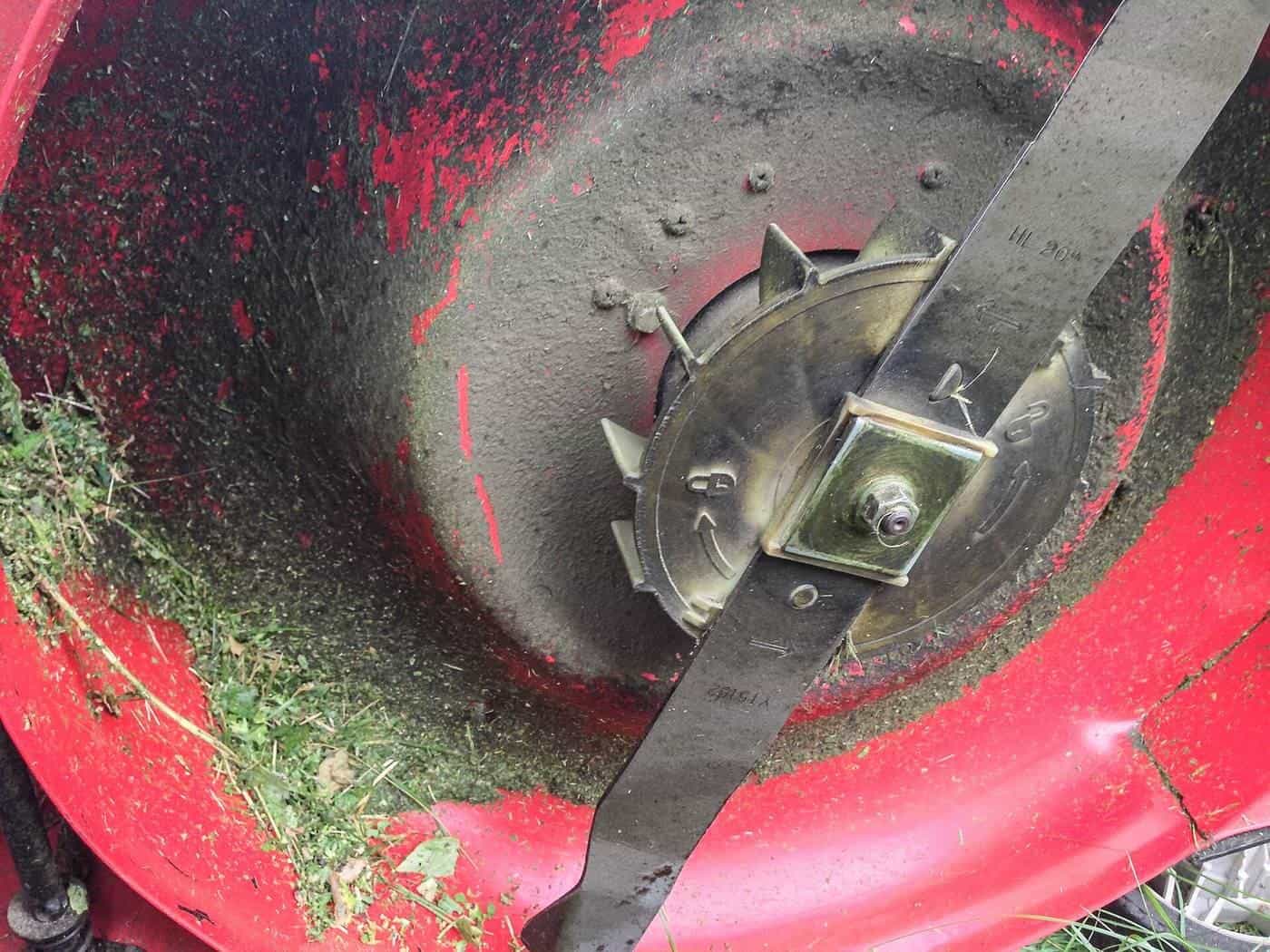 The underside of a red mower deck showing the blade and grass clippings