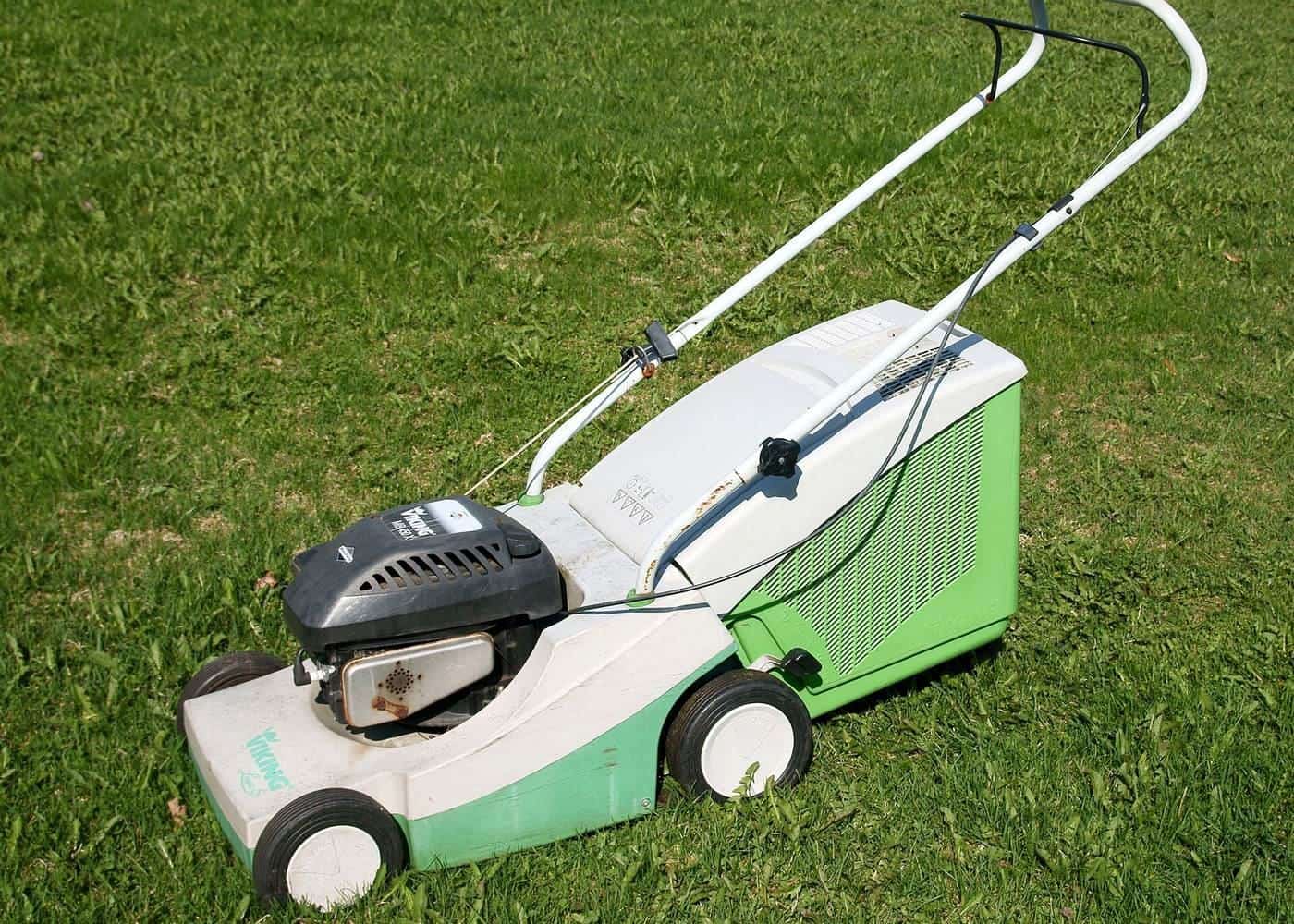 A white and green battery lawn mower standing on a lawn