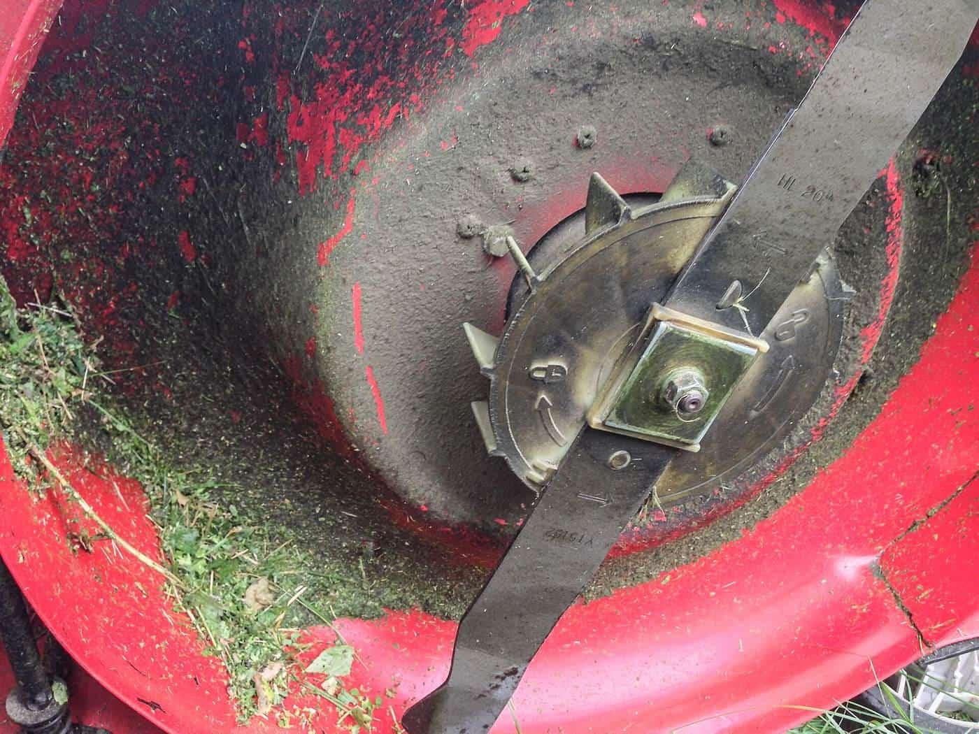 The underside of a red mower deck showing the blade and grass clippings